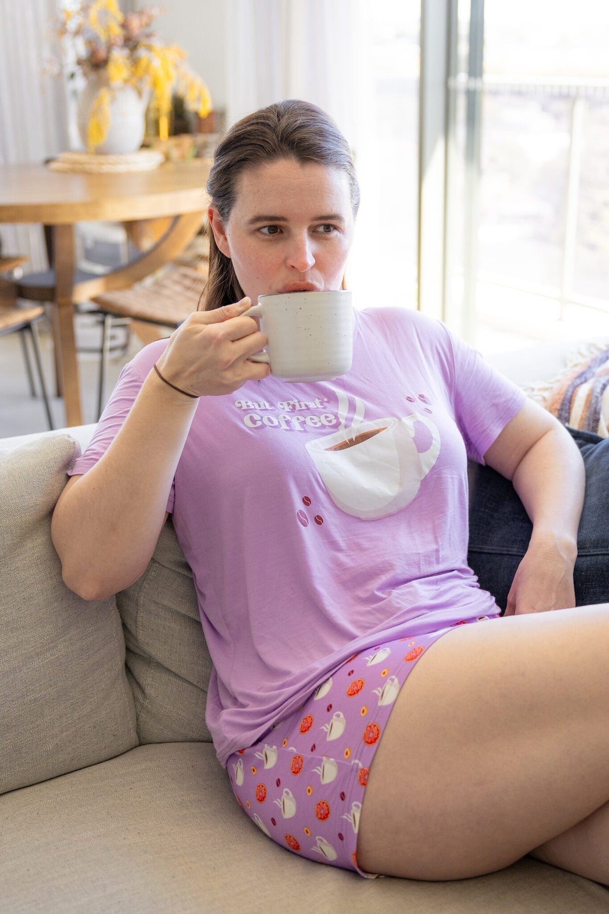 Woman wearing the Rest Day PJ But First Coffee lilac pyjama set, three-quarter view with coffee mug